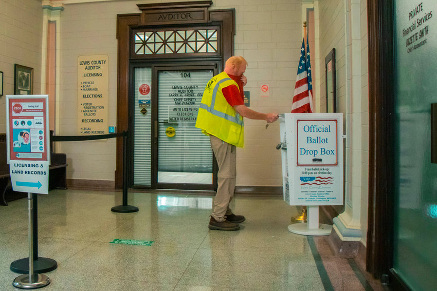 A man uses his shirt to cover his face as he drops his ballot off at a ballot box in the Lewis County Courthouse during the primary election in August.