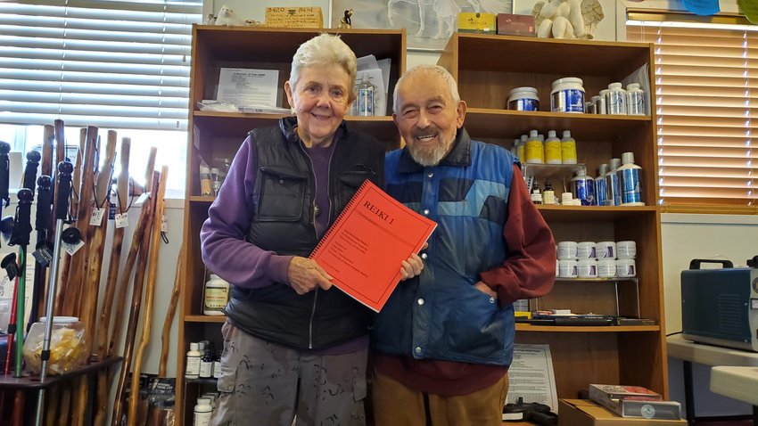 Taylore and Roi Vance standing in their studio classroom holding the Reiki level one handbook, which is what all beginners to their classes start their training with.