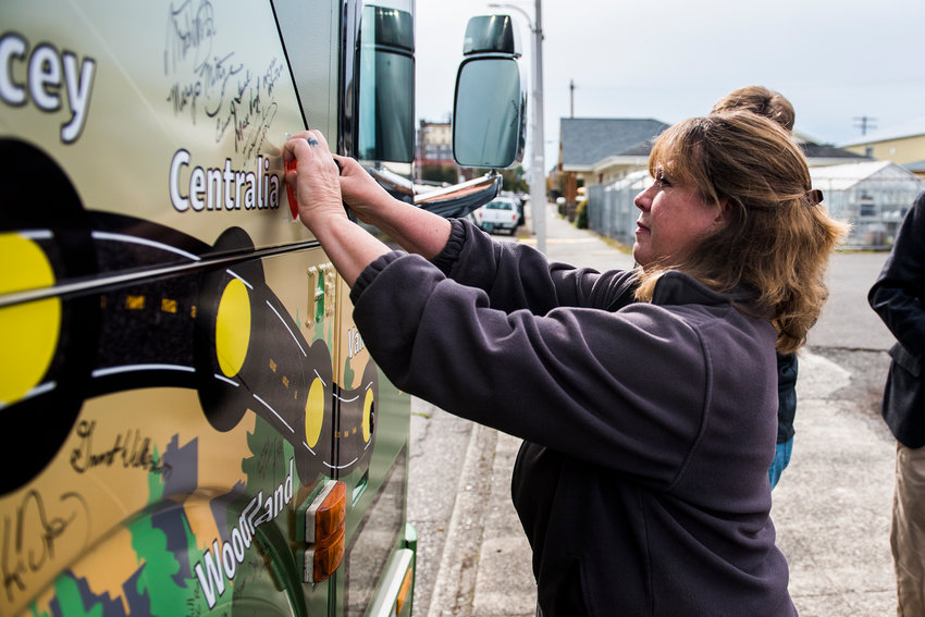Andrea Churchill puts a Churchill Glove Co. sticker on the outside of an Association of Washington Business bus during a Manufacturing Week event in Centralia in 2018.