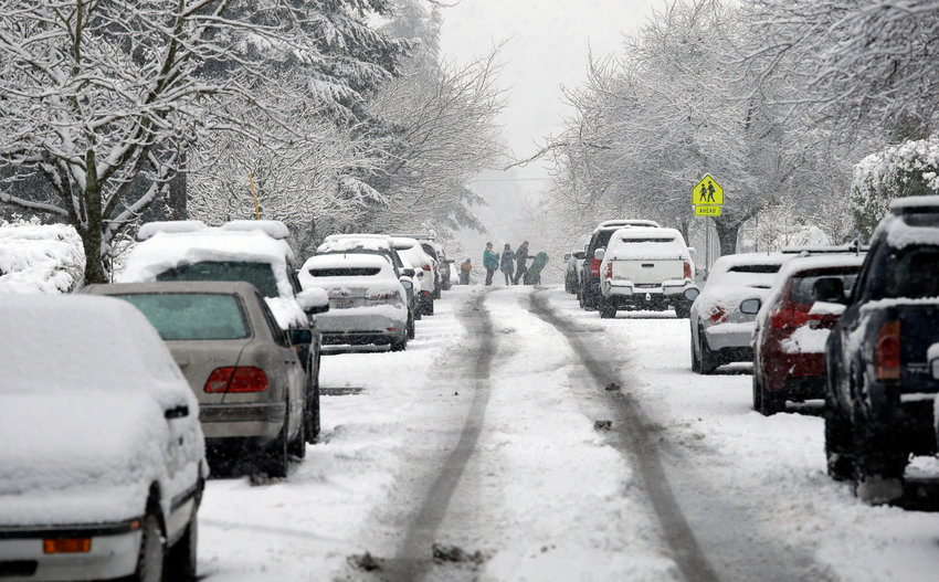 Snow covers streets and trees as pedestrians make their way through a winter storm.