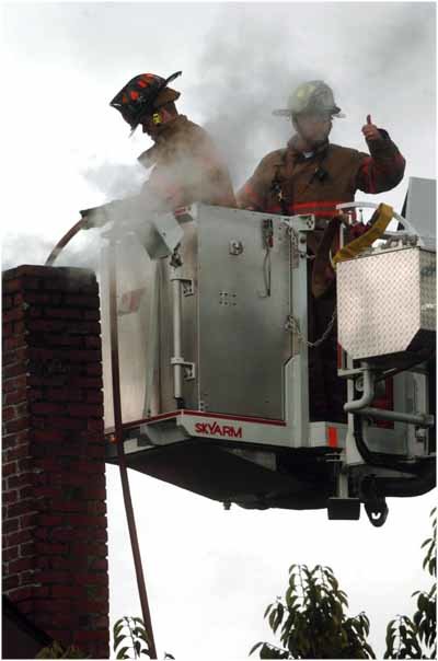 Alex Sutherland / The Chronicle  Capt. Rob Gebhart lowers a fire hose into a burning chimney while his Chehalis Fire Department partner, Casey Beck, signals the bucket operator below on Wednesday morning at a Chehalis home.