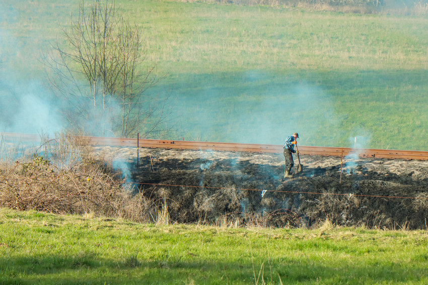A man uses a shovel as brush near train tracks smolders after a brush fire was called in Wednesday near Adna.