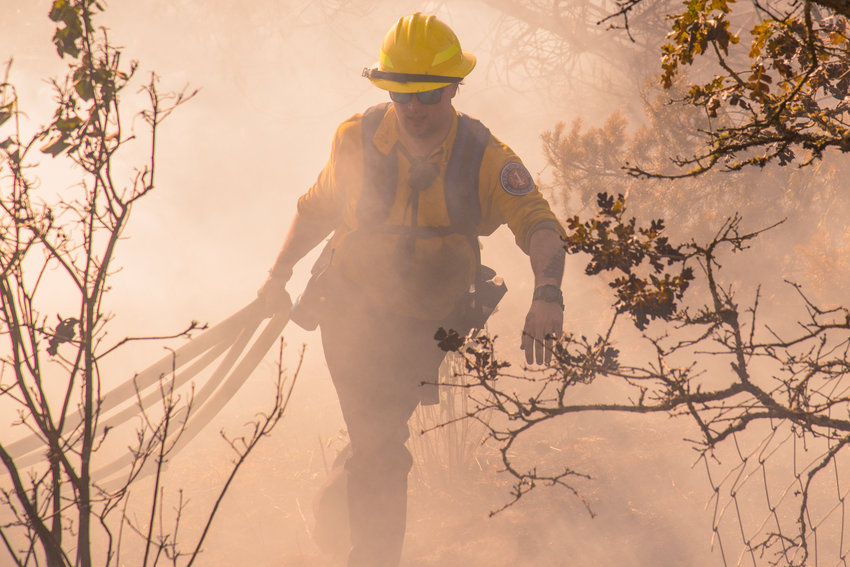 A member of West Thurston Regional Fire Authority carries hoselines through smoke during a brush fire in the Scatter Creek area near Case Road in Maytown in July 2021.