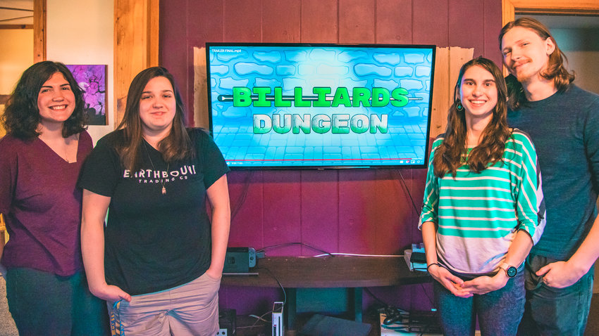 From left, marketer Sheila Johnson, artist Calista Brasher, marketing manager Catherine Cleveland and game designer William Cleveland smile for a photo in front of the logo for their company&rsquo;s new game, &ldquo;Billiards Dungeon,&rdquo; which will be released on July 30.