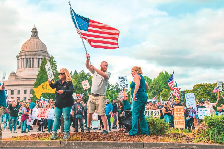 Sean Bresnahan, co-founder of Medical Freedom Lewis County, stands in the median strip of Capitol Way South while waving an American Flag Saturday afternoon during a &quot;Stop the Mandate&quot; protest in Olympia.