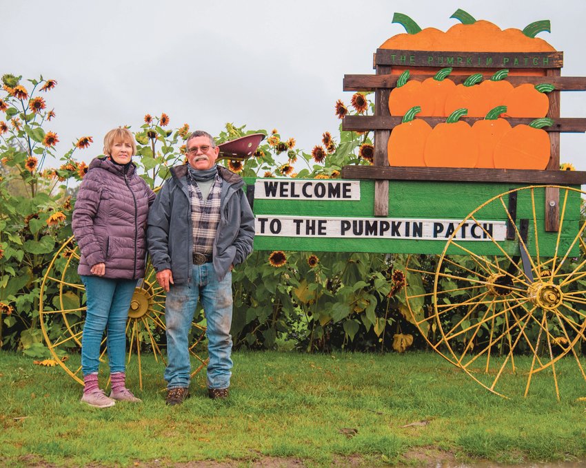 Linda and Tim Crockett smile and pose for a photo in front of wagon shaped signage for their pumpkin patch off Goodrich Road in Centralia Thursday morning.