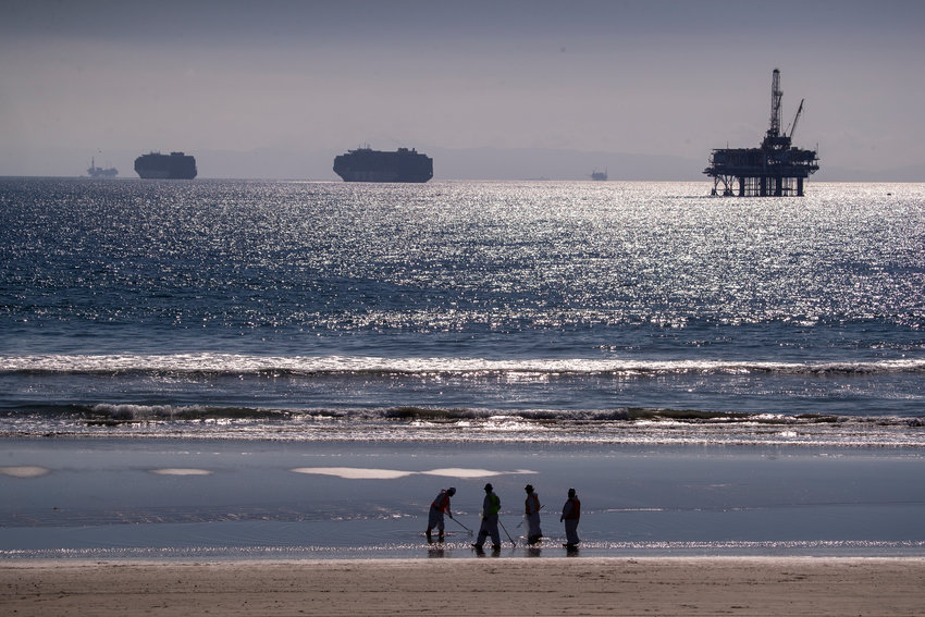 Container ships and an oil derrick line the horizon on Tuesday, Oct. 5, 2021, as environmental oil spill cleanup crews search the beach, cleaning up oil chunks from a major oil spill in Huntington Beach, California. (Allen J. Schaben/Los Angeles Times/TNS)