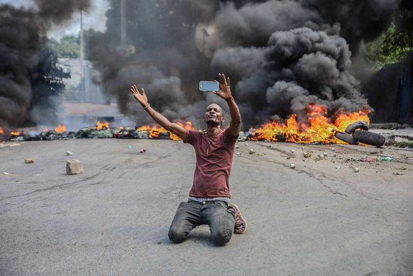 A man films himself in front of tires on fire during a general strike launched by several professional associations and companies to denounce insecurity in Port-au-Prince, Haiti on Monday, Oct. 18, 2021.(Richard Pierrin/AFP/Getty Images/TNS)