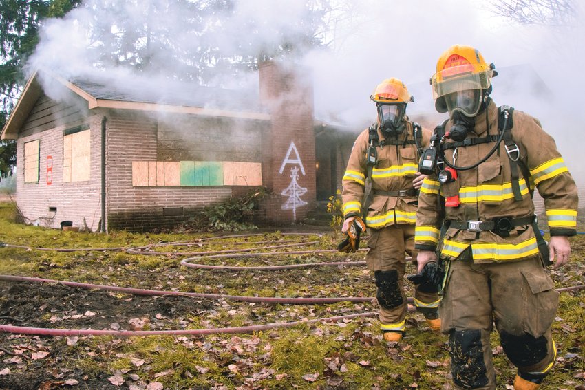 Smoke rises from a building, as firefighters walk by gloves in hand, during a practice burn on a house located at Tahoma Boulevard and Berry Valley Drive in Yelm Saturday morning.