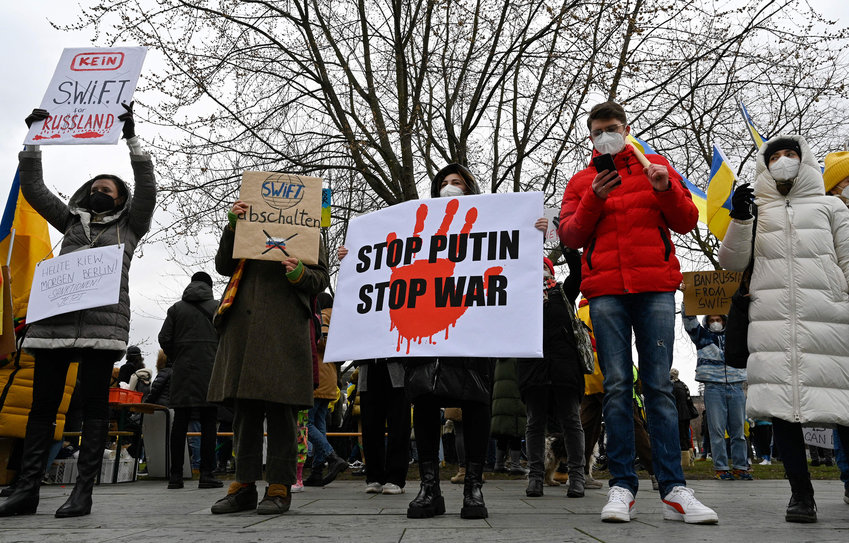 Demonstrators hold placards reading, from left, &quot;No SWIFT for Russia,&quot; &quot;Turn off SWIFT,&quot; &quot;Stop Putin, Stop War&quot; during a protest against Russia's invasion of Ukraine on Feb. 25, 2022, in front of the Chancellery in Berlin. (John MacDougall/AFP/Getty Images/TNS)