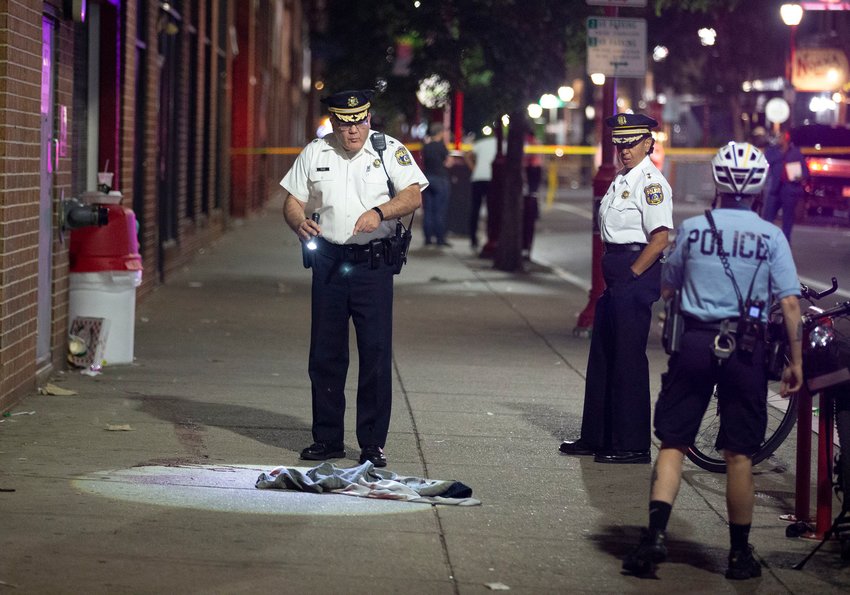 Philadelphia police officers and detectives look over the evidence at the scene of a shooting on and near South Street that left three dead and 11 wounded late Saturday. (Charles Fox/The Philadelphia Inquirer/TNS)
