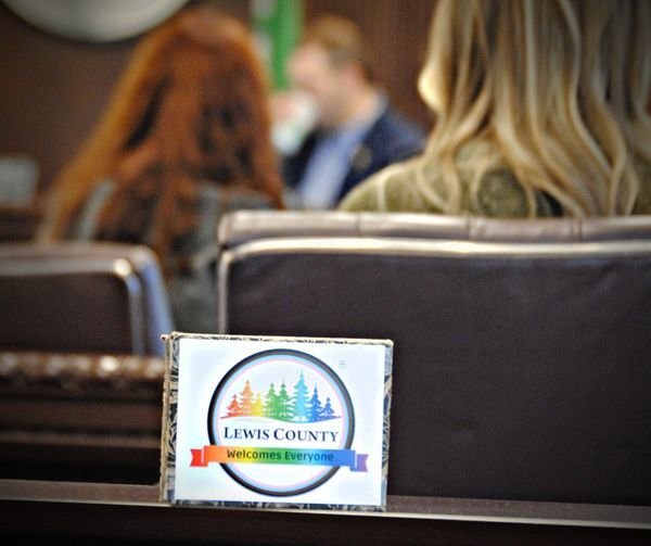 An altered version of the Lewis County logo reads &ldquo;Lewis County Welcomes Everyone&rdquo; during a meeting.