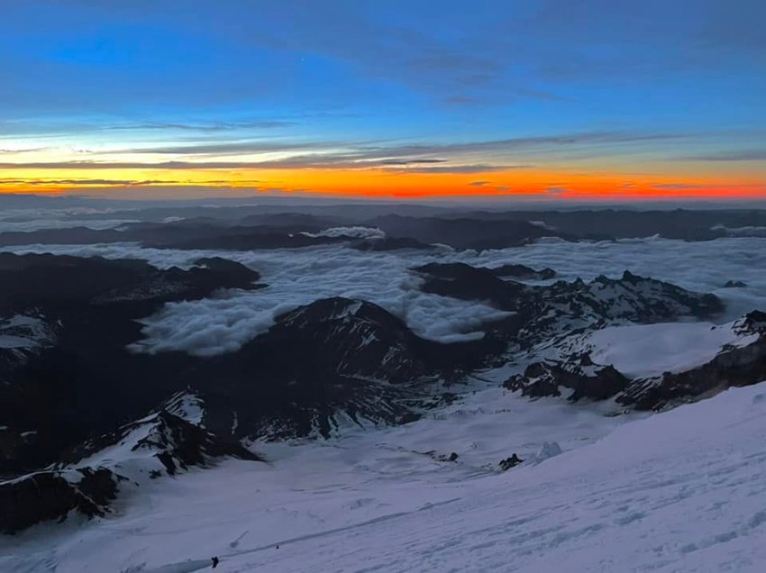 Clouds hang around foothills of Mount Rainier as an orange sky is seen above at sunrise.