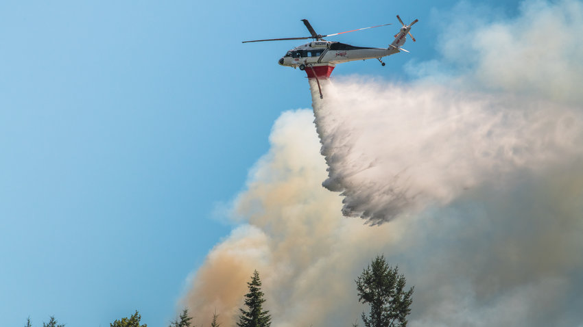 A Department of Natural Resources helicopter flies over a forest fire in Bucoda while dropping water Monday afternoon near the intersection of Highway 507 and Troy Avenue.
