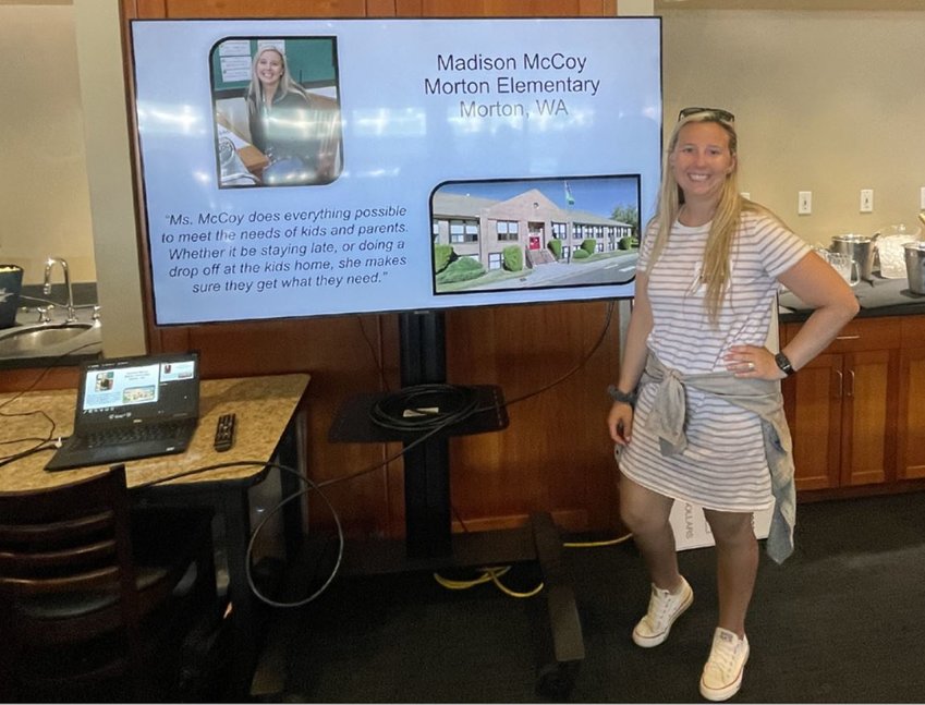Morton Elementary School third grade teacher Madison McCoy stands in front of a screen showing an excerpt from her nomination for WSECU Teacher of the Week.