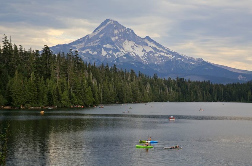 Kayaks, rowboats and paddle boards take to Lost Lake on a cloudy summer day, with Mount Hood in the near distance.