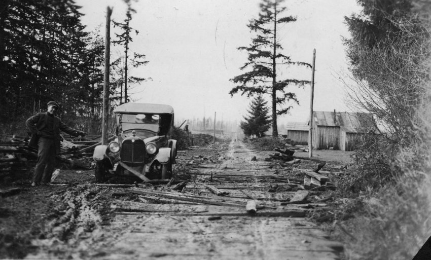 This 1919 photo was made into a postcard and sent to Miss Frede Erickson (aunt of the contributor). The note reads: &quot;Dear Friend: Received your letter. Glad to hear from you. Here I send you a picture of the beautiful highway between Centralia and Portland. I was down that way last Monday. We had some time through the mud holes. We are all all right and working in the shipyard. The signature on the postcard has been cut off. This so-called puncheon road used slabs from the mills to help eliminate the hazards of traveling through mud &mdash; unless, of course, drivers like this one went around them and got stuck.
