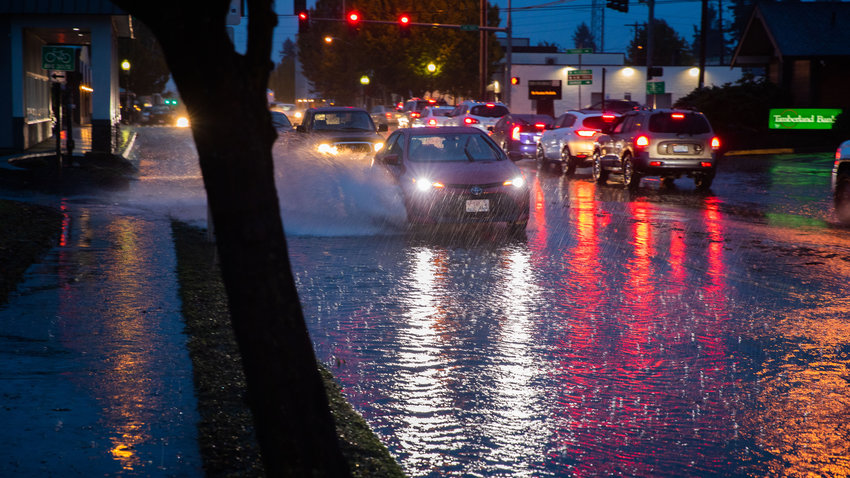Vehicles drive through water over the roadway along West Yelm Avenue on Friday night as rain falls.