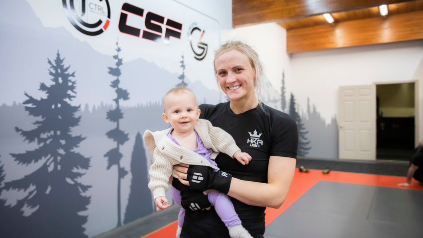 Kayla Weed, a W.F. West graduate, smiles for a photo while holding her 1-year-old daughter Mia inside Combat Sport and Fitness in Enumclaw on Thursday while training for her upcoming fight on March 11, at the Muckleshoot Casino.