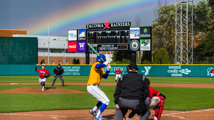 Tenino&rsquo;s Cody Strawn (2) throws a pitch to Rochester&rsquo;s Hyde Parrish (8) as a rainbow forms over Cheney Stadium, home of the Tacoma Rainiers, on April 1.
