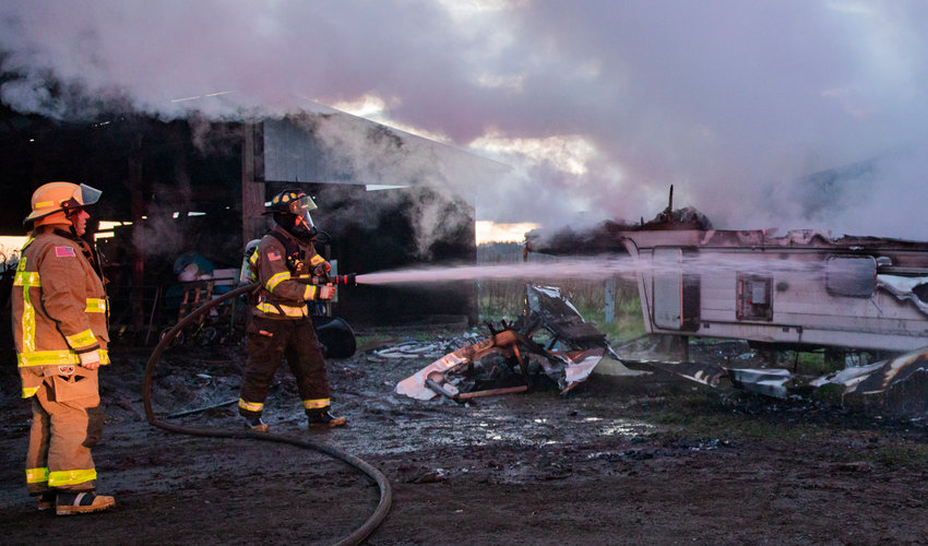 Firefighters from Salkum and Mossyrock work to keep back a fire from a shed in Salkum that destroyed a trailer along Fuller Road on Wednesday night.