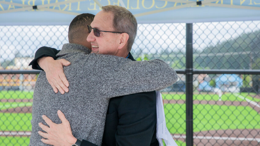 Bob Peters smiles as he gives Assistant Athletic Director Jonathan McMillan a hug following a speech made in his honor during a field dedication ceremony at Centralia College on Monday, May 22.