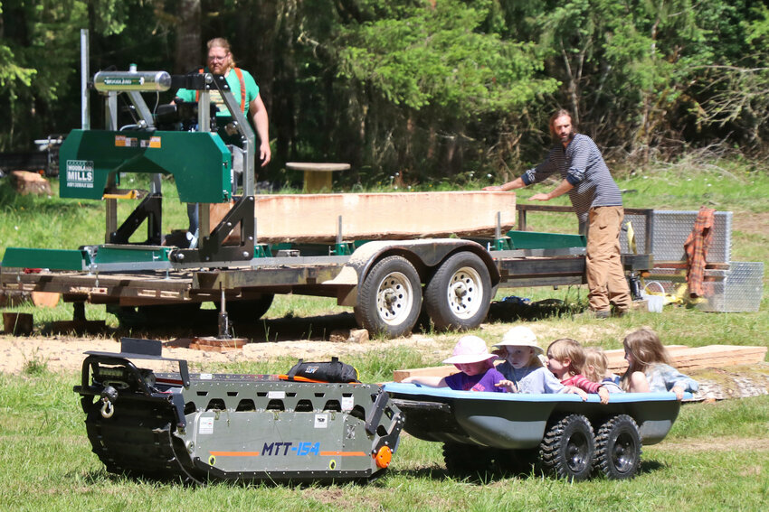 An MTT-154 autonomous vehicle pulls a wheelbarrow full of children past a sawmill, operated by Jake Dailey and Boone Bergsma, at Camp Singing Wind near Toledo on Sunday, June 11.