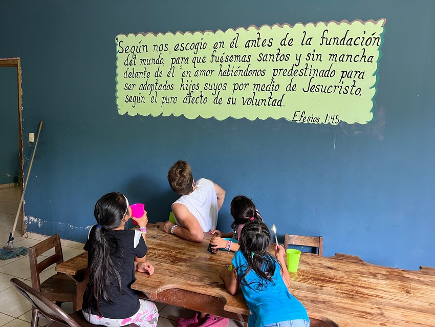 At the giggling request of girls living at Heart 2 Heart Children's Village in Honduras, Sam Mittge reads a Spanish language Bible passage painted on the wall in the girls' dining area on June 22, the third day of a 10-day missions trip led by Bethel Church to serve and show love to the mostly orphaned or abandoned children who have been  there. Roughly translated, the verse reads: &quot;Even before he made the world, God loved us and chose us in Christ to be holy and without fault in his eyes. God decided in advance to adopt us into his own family by bringing us to himself through Jesus Christ. This is what he wanted to do, and it gave him great pleasure.&quot;
