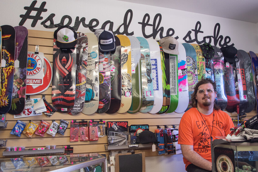 Kraken Board Shop founder Braden Allee sits in front a display of skateboard decks for sale on Thursday.