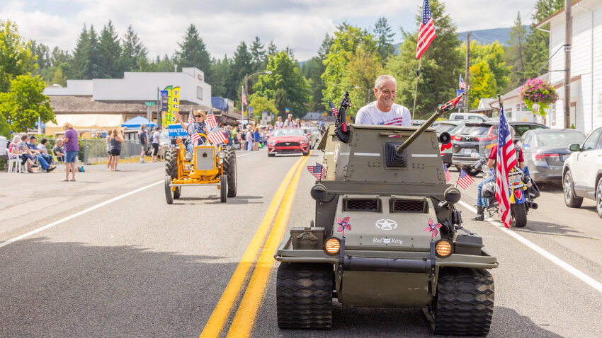 Senator Jeff Wilson smiles from inside a miniature tank while riding through Ryderwood during centennial celebrations on Saturday, July 29.