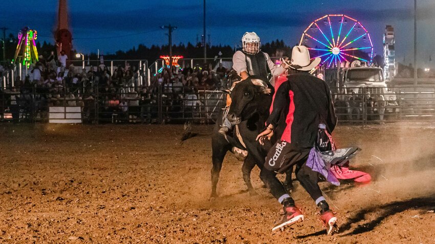 A rodeo clown moves around a bull and its rider inside the Grandstand Arena during the Southwest Washington Fair rodeo in 2022.