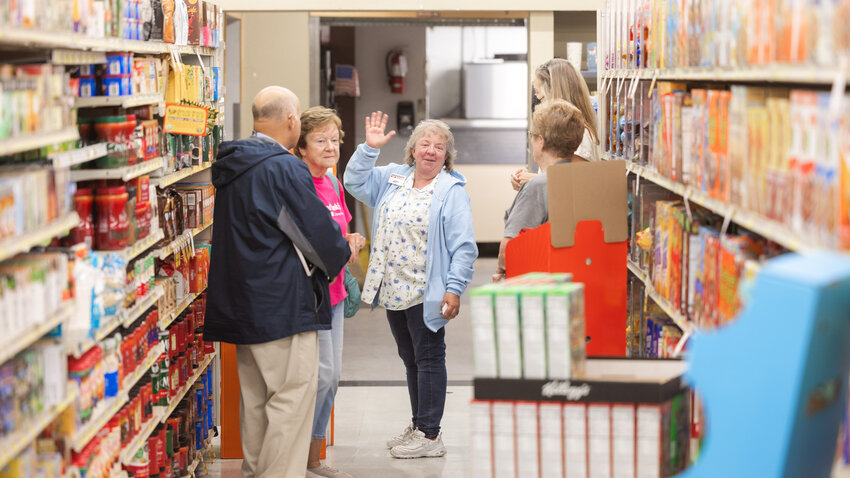 Tenino Food Bank Plus Executive Director Jody Stoltz, a Tenino resident originally from Doty, smiles and waves to the camera while placing tags on store items that are preferred by the food bank as donations on Tuesday, Aug. 22, at Tenino Market Fresh.