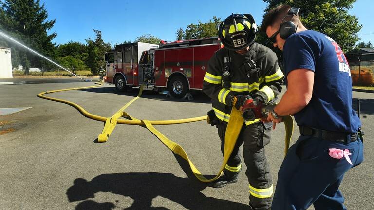 Lt. Evan Parnell assists firefighter Christian Valdez while firefighter Ryan Fakkema monitors the water spray during an &ldquo;Evolution&rdquo; training drill at the South Bay Fire Department&rsquo;s training center on August 2, 2023.