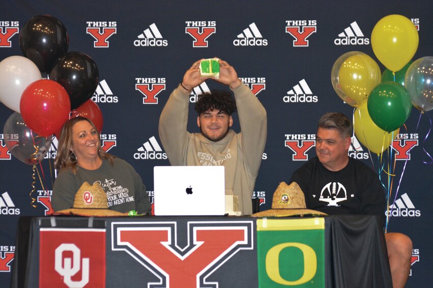 Brayden Platt, with his parents Rachel and Cy, officially commits to the University of Oregon by holding a Ducks&rsquo; colored piece of cake in the air.