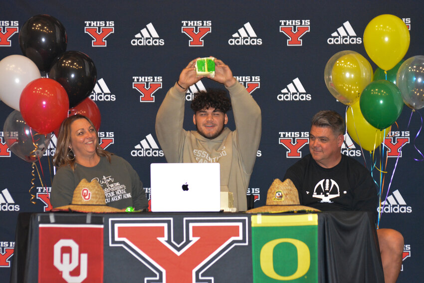 Brayden Platt, with his parents Rachel and Cy, officially commits to the University of Oregon by holding a green and yellow piece of cake in the air.