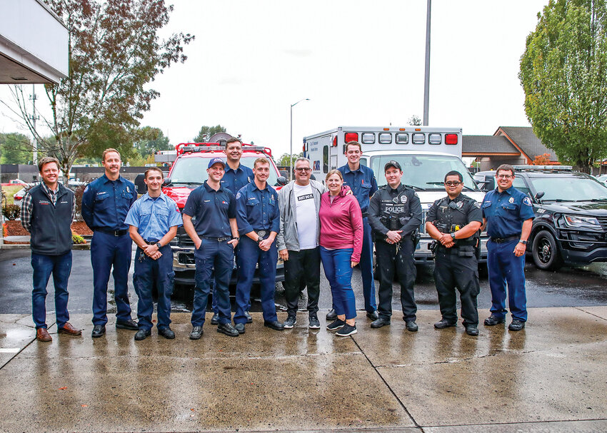 First responders stand with cardiac arrest survivor Brad Ruff and wife Gretchen Ruff, center. From left to right, Dr. Jason Hanley, MD &mdash; PeaceHealth, Fire District 3 firefighter Tim Axelson; Kaden Shropshire &mdash; American Medical Response; American Medical Response paramedic Tanner Elliott; Fire District 3 Capt. Josh Hall; Fire District 3 firefighter/paramedic Jerik Traffie; Brad Ruff; Gretchen Ruff; Fire District 3 intern Trey Bowman; Battle Ground Police officers Max Everett and Jeff Cabanting-Rafael; and Fire District 3 firefighter Kirk Meller.