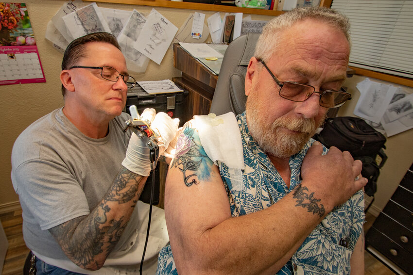 Nic Ettner sits in Skindoodle Tattoo's studio in Chehalis while studio owner Michael Cristina does touch up work to a fadded piece on his shoulder on Oct. 19.