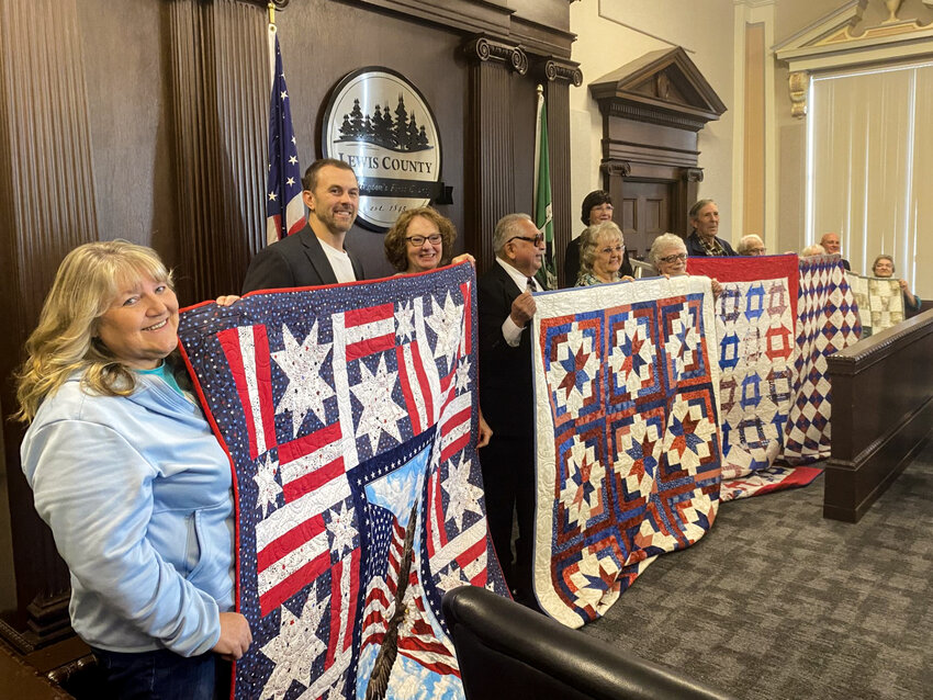 Lewis County commissioners Sean Swope, Lindsey Pollock and Scott Brummer stand behind quilts that will be given to veterans alongside volunteers from the Veterans Memorial Museum Quilts of Valor chapter.