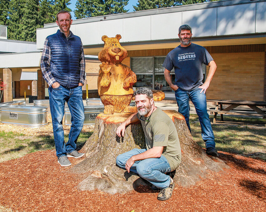 Pleasant Valley School Principal Craig Pearson stands with wood-carving twins Patrick and Mike Bryson with their piece, Buddy the Beaver.