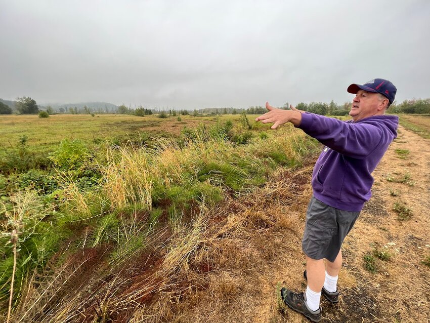 Bob Russell, standing atop the levee south of the Southwest Washington Fairgrounds in August 2023, points to the area where Coal Creek empties into Salzer Creek after running through property owned by the city of Chehalis.