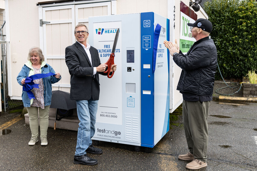 Tenino Mayor Dave Watterson cuts the ribbon for the new free health care kiosk at the Tenino Food Bank Plus on Tuesday, Feb. 20, as Thurston County Commissioner Wayne Fournier and Tenino Community Service Center Executive Director Jody Stoltz  look on.