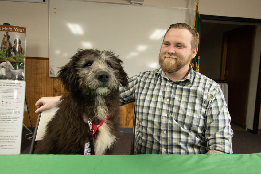 Clyde, the Lewis County &quot;Director of Fluff&quot; and resident veteran therapy dog for the county, sits next to Veterans Journey Forward director and U.S. Marine Corps veteran Jesse Lloyd on Saturday, March 23, at the Veterans Stand Down in Randle.
