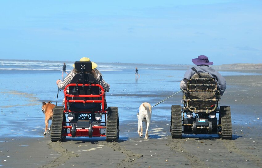 A pair of guests make their way down Westport beach using tracked mobility chairs from David&rsquo;s Chair, a nonprofit partnering with the city to help bring the beach to more people.