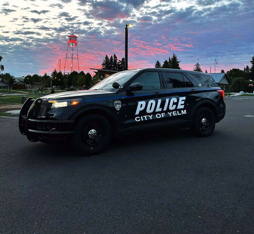 A Yelm police vehicle sits in front of a cotton candy-colored sky near the Yelm Water Tower.