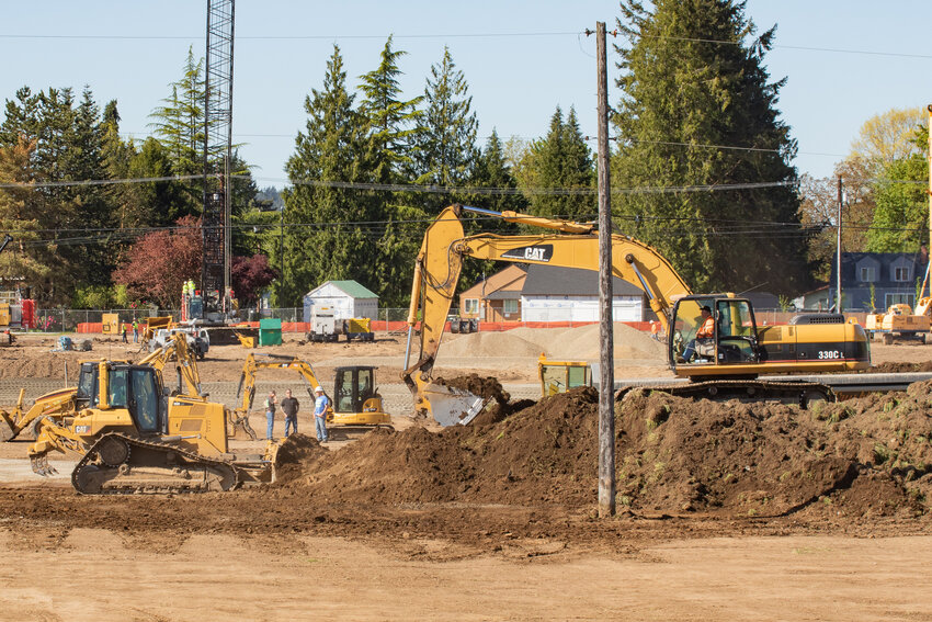 A bulldozer pushes dirt toward a pile where an excavator waits to put the dirt into dump trucks to be hauled off of the WinCo Foods construction site at Centralia Station on Thursday, May 9.