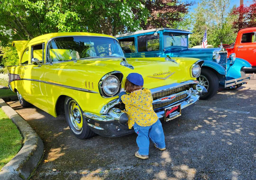 A child checks out a bright yellow Chevrolet Bel-Air during the 2023 Coats for Kids Car Show in Yelm.